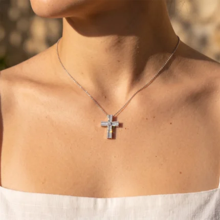 Silver cross pendant necklace with rhinestones on a thin silver chain resting on the collarbone.