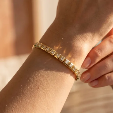Gold bracelet with square, diamond-encrusted links on a bare wrist in warm light.