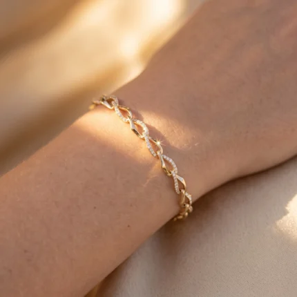 Close-up of a gold bracelet with diamond-studded links worn on a wrist against a soft beige background.