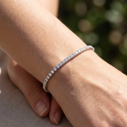 Close-up of a wrist wearing a silver diamond tennis bracelet in sunlight, highlighting the stones' sparkle.