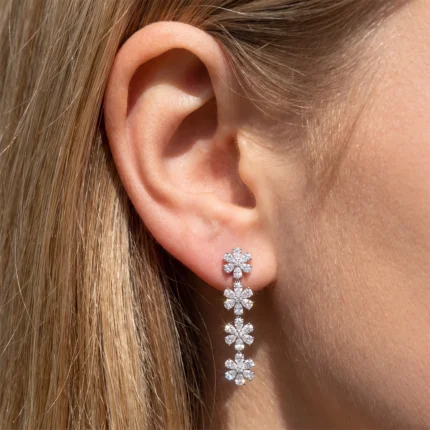 Close-up of an ear wearing a diamond flower drop earring with linked blossom motifs along a chain.