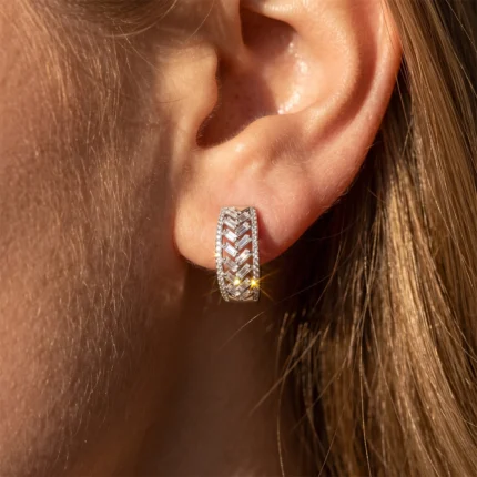 Close-up of a silver diamond-studded hoop earring with a zigzag pattern on the earlobe and hair in the background.