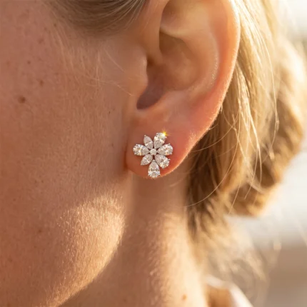 Close-up of a flower-shaped diamond earring on the earlobe, with multiple clear stones sparkle.