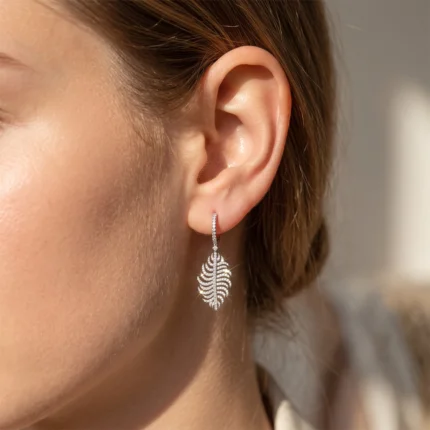 Close-up of a woman's ear wearing a diamond-studded silver leaf-shaped drop earring.