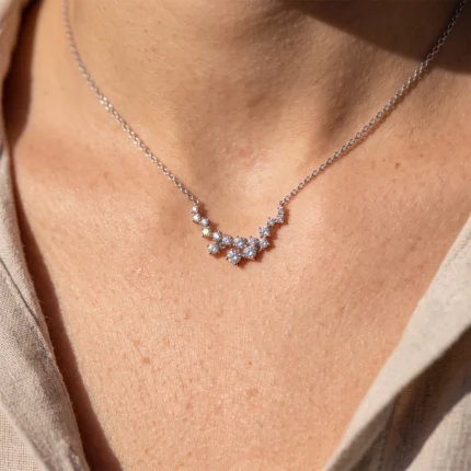 Close-up of a silver diamond necklace resting on a woman's collarbone with pavé-set stones in a V-shaped cluster.