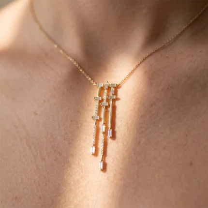 Gold pendant necklace with dangling vertical bars and diamond accents on a woman's bare neck and décolletage.