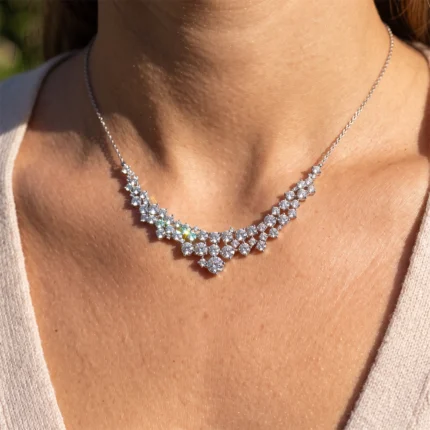 Close-up of a diamond necklace with starburst clusters worn on a woman's neck, catching sunlight on a beige top.