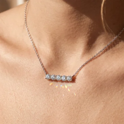 Diamond bar necklace with five round diamonds resting on a woman's collarbone area in sunlight