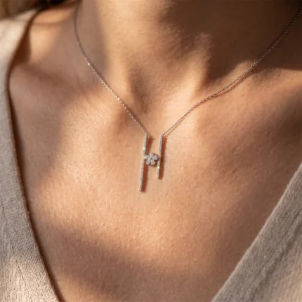 Silver necklace with two vertical bar pendants and a central flower-shaped diamond cluster resting on the collarbone.
