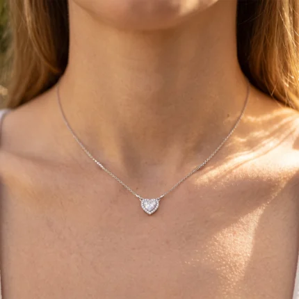 Silver heart pendant necklace resting on a woman's collarbone, sparkly stones around the heart in sunlight