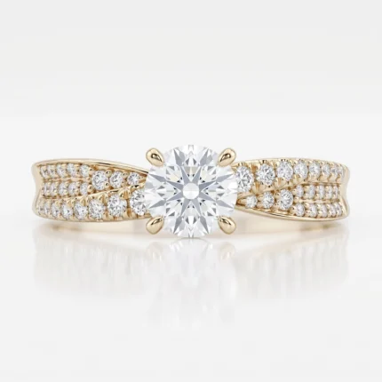 Gold ring featuring a large round center diamond in a four-prong setting with pavé diamonds along the band, on a reflective white surface.