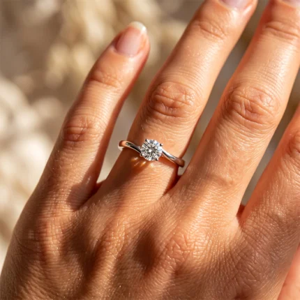 Close-up of a hand wearing a silver solitaire engagement ring with a round diamond on the ring finger
