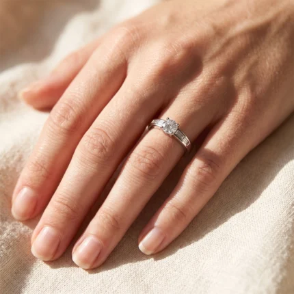 Close-up of a woman's left hand showing a silver solitaire diamond engagement ring on the ring finger.