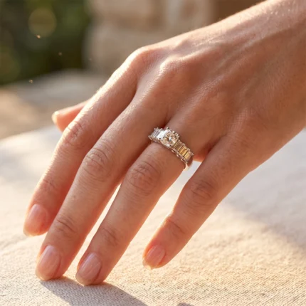 Close-up of a hand wearing a princess-cut diamond engagement ring with a two-tone band and side stones on warm sunlight.