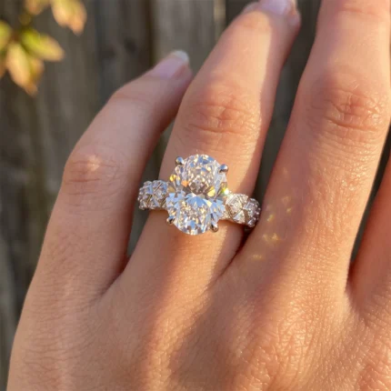 Close-up of a diamond engagement ring with a large center stone and pavé band on a finger, warm sunlight reflecting off the stones, gold setting