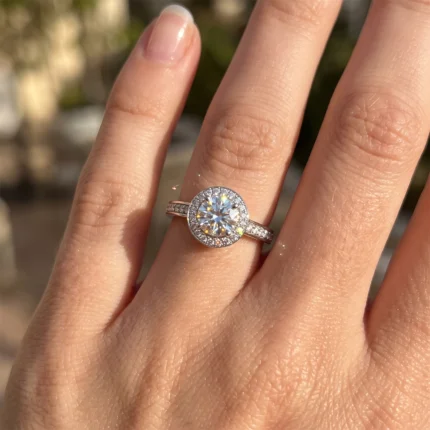 Diamond halo engagement ring on a finger, with a large central stone and pavé band in sunlight.