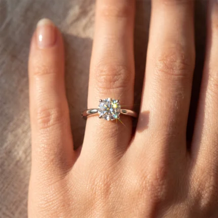 Close-up of a diamond engagement ring on the ring finger sparkling in sunlight.