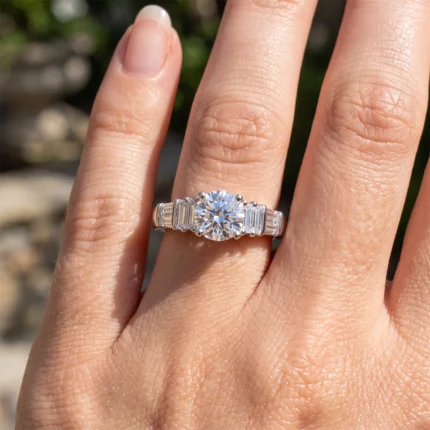Close-up of a diamond engagement ring on a finger, featuring a large round center stone with baguette-side stones on each side.