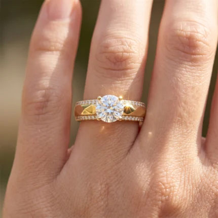 Gold ring with a large round-cut center diamond and two diamond-studded bands on a finger, featuring gold pyramid accents on the sides.