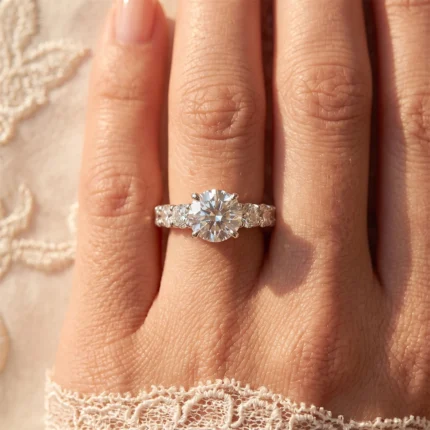 Close-up of a woman's hand wearing a diamond engagement ring with a large round center stone and smaller stones along the band.