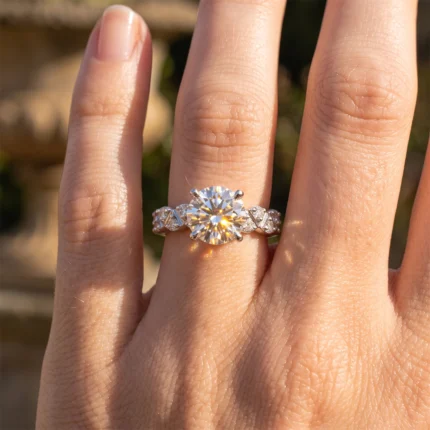 Close-up of a hand wearing a diamond engagement ring with a large central stone and pavé-accent band in sunlight.