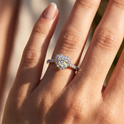 Close-up of a hand wearing a heart-shaped diamond engagement ring with a pavé band on the ring finger.