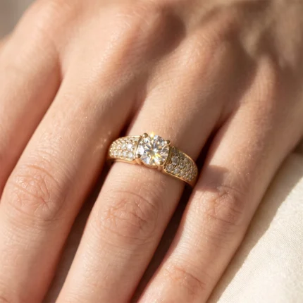 Gold ring with a large central diamond and pavé-set diamonds along the band worn on a finger.