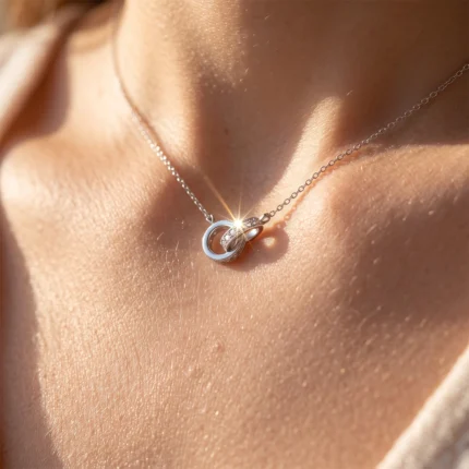 Close-up of a silver layered pendant necklace resting on a woman's bare neck with a sun glare on the rings