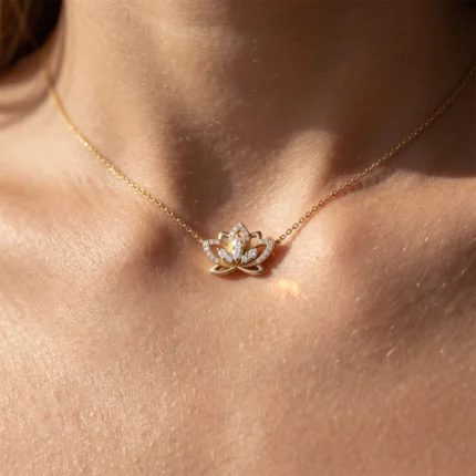 Gold chain necklace with a diamond-encrusted lotus pendant resting on a bare décolletage, close-up.