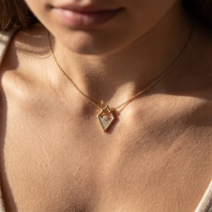 Gold necklace visible on the skin with a diamond-shaped pendant, featuring a small round diamond inside a hollow frame at the center of the chest.
