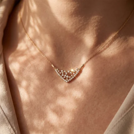 Gold chain necklace with a diamond-studded fan-shaped pendant resting on a woman's collarbone, catching the light.