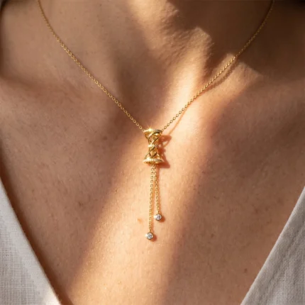 Gold necklace with a spiraled pendant and two dangling gem-accented chains on a bare neck.