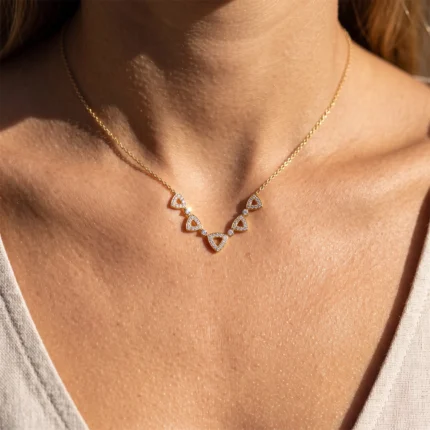 Gold chain necklace with a row of diamond-trimmed hollow triangular pendants resting on a woman's neckline.