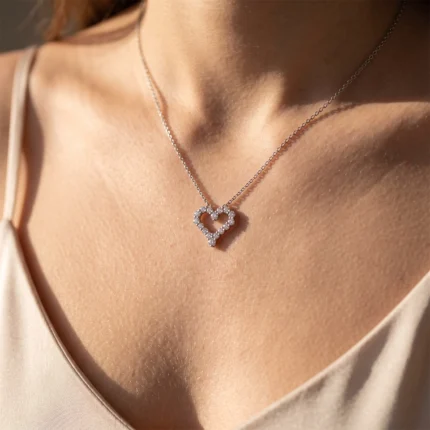 Silver heart pendant necklace with small rhinestones resting on a woman's décolletage.