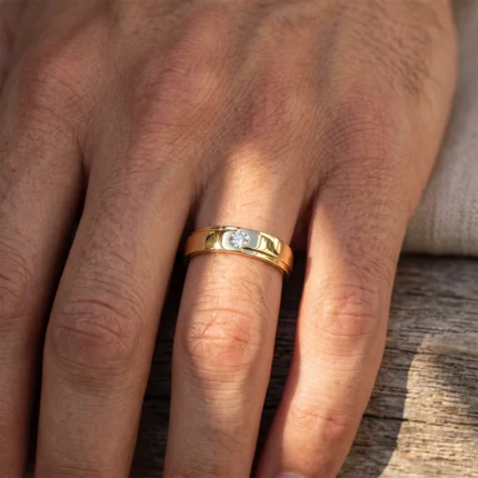Close-up of a gold ring with a small round diamond on a finger, resting on a wooden surface.