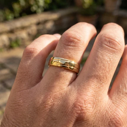 Close-up of a gold wedding band on the ring finger, with sunlight reflecting off the polished surface.