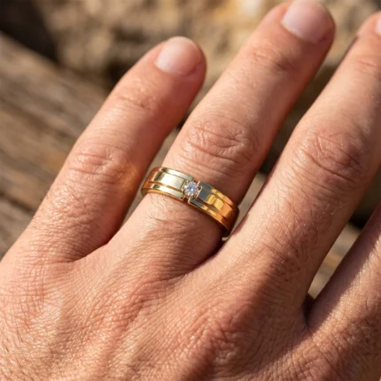 Close-up of a hand wearing a two-tone gold and silver ring with a small diamond on the ring finger.