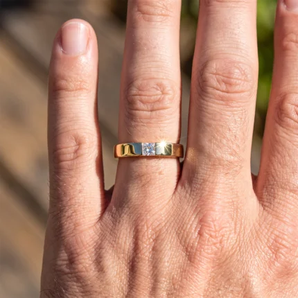Close‑up of a hand wearing a gold band with a central diamond, sunlight creating a sparkle on the gem.