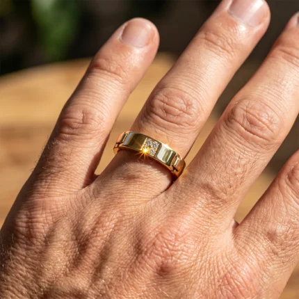 Close-up of a gold ring with a diamond centerpiece on the ring finger of a hand, sunlight reflecting off the gem.