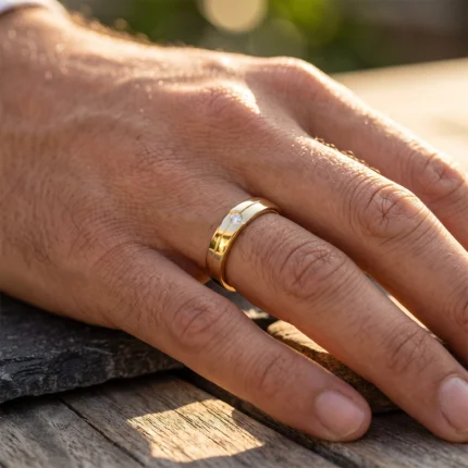 Close-up of a hand resting on a wooden surface, wearing a two-tone gold ring with a small diamond set in the band, bathed in warm sunlight.