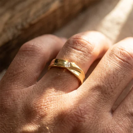 Close-up of a gold ring with a small square diamond on a finger, sun catching the facets.