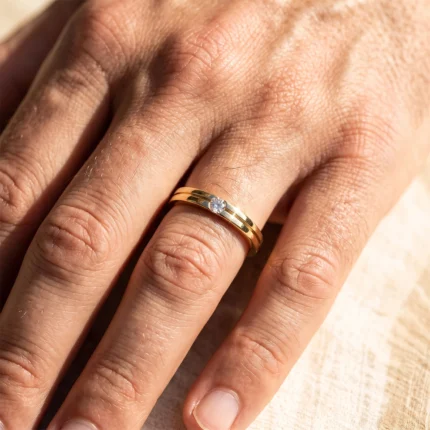 Close-up of a hand wearing a gold two-band ring with a single diamond on the ring finger.