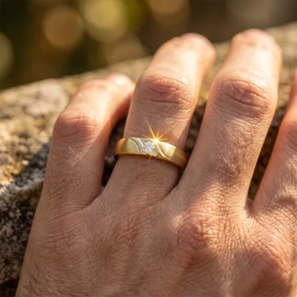 Close-up of a gold ring with a single diamond on the finger, sunlight making the diamond sparkle.
