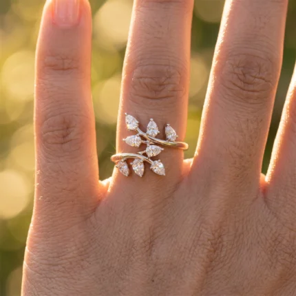 Hand with a gold leaf-like diamond ring stack on the ring finger, sunlit and blurred background.
