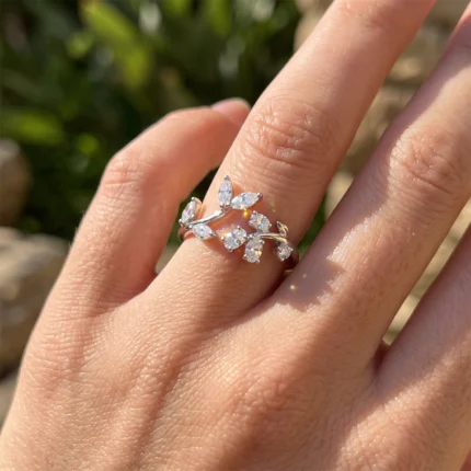 Delicate silver ring shaped like a vine with marquise-cut diamonds on the finger, outdoors in sunlight.