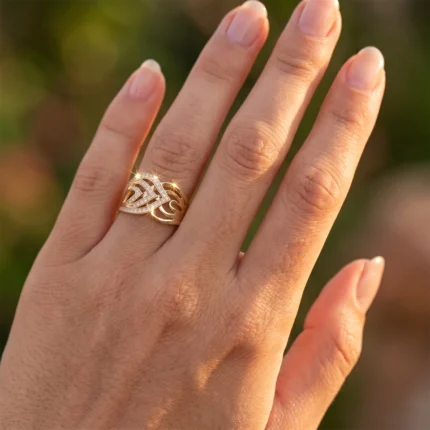 Close-up of a hand wearing a gold interwoven band ring with diamond accents on the ring finger.