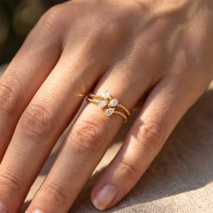Close-up of a hand wearing two delicate twisted gold rings with three heart-shaped diamonds on the top ring, on the ring finger