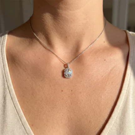 Silver necklace with a square halo pendant featuring a central rectangular diamond, resting on a light top.