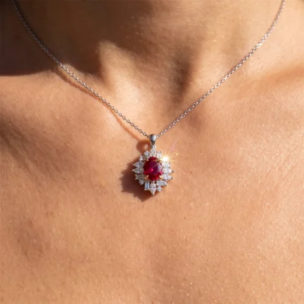 Pendant necklace with a red oval ruby center, surrounded by a halo of diamonds in a sunburst design on a delicate silver chain.