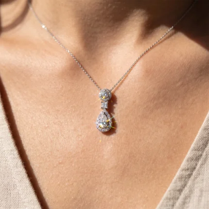 Silver necklace with a sparkling round diamond bead connected to a teardrop-shaped diamond pendant resting on bare skin at the neckline.